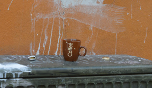 Fotografi af et skåret kaffekrus på et telefonskab med ølkapsler.